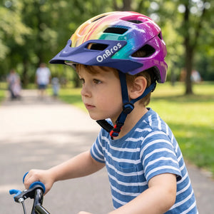 A little boy wearing a rainbow colored helmet is riding a bicycle