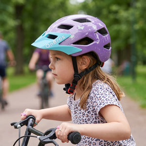 A little girl wearing a purple helmet is riding a bicycle